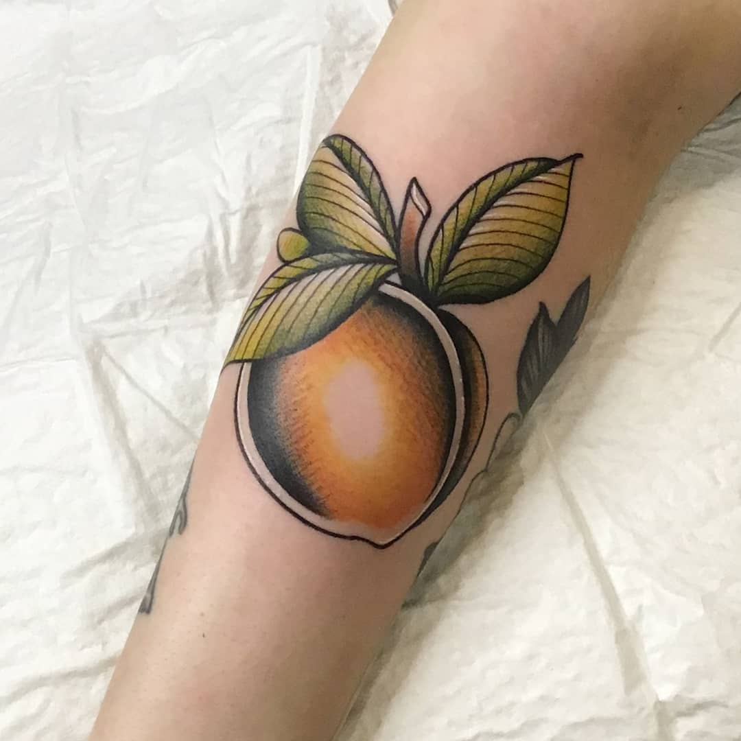 Tattoo of a peach with leaves on someone's leg